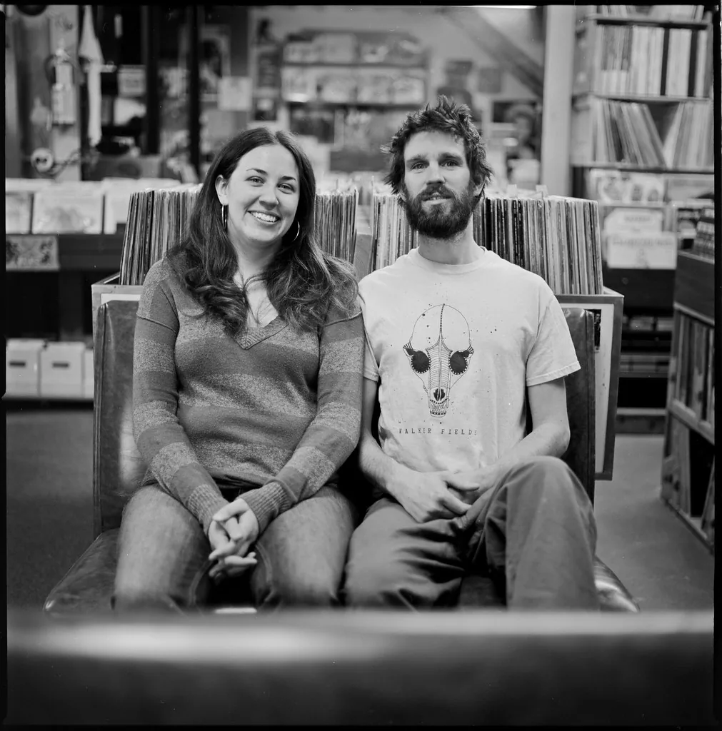 Two people sitting in front of rows of vinyl records Two people sitting in front of rows of vinyl records